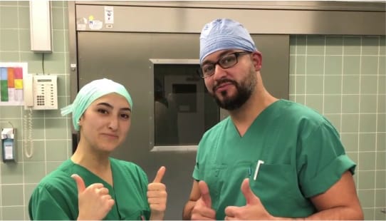 Doi asistenți medicali îmbrăcați în verde, bărbat și femeie care se află într-o sală de operații.